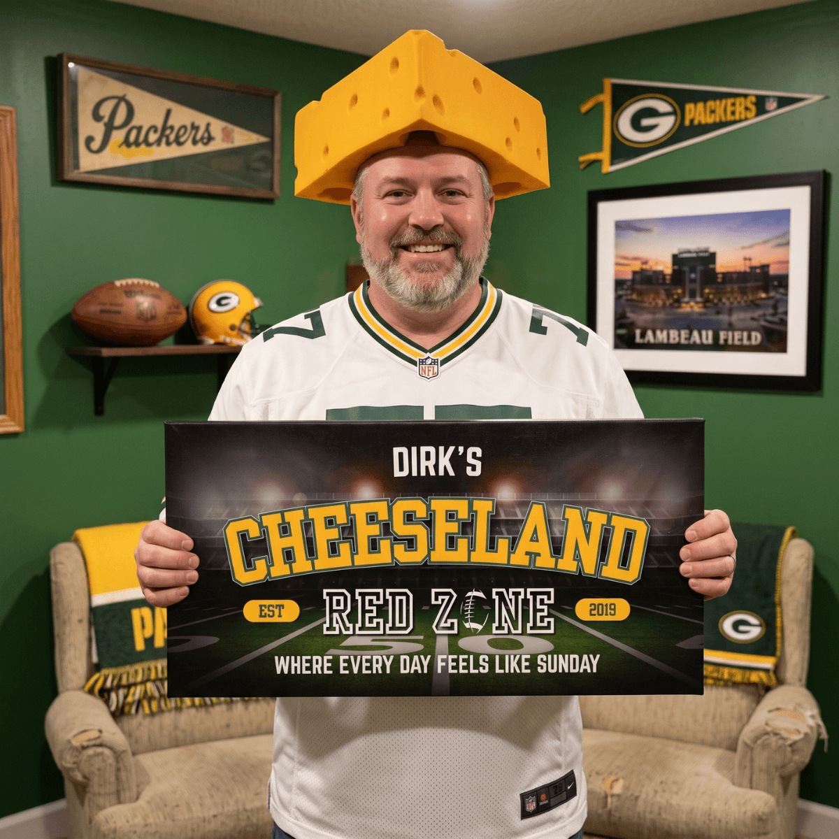 Man holding a personalized Green Bay Football Sign in a man cave, wearing a cheese hat and showcasing team spirit.